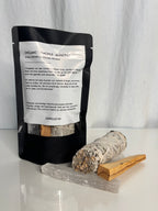 zu sehen ist einer verpackung, mit Palo Santo holz, Salbei und selenit Kristall davor, auf der verpackung steht ein mantra