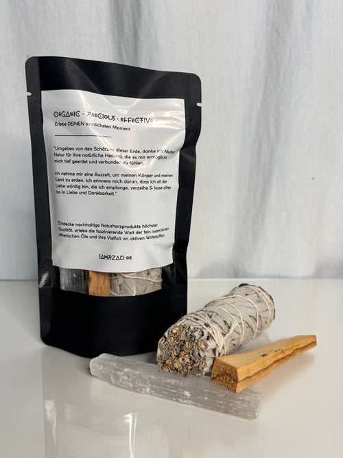 zu sehen ist einer verpackung, mit Palo Santo holz, Salbei und selenit Kristall davor, auf der verpackung steht ein mantra