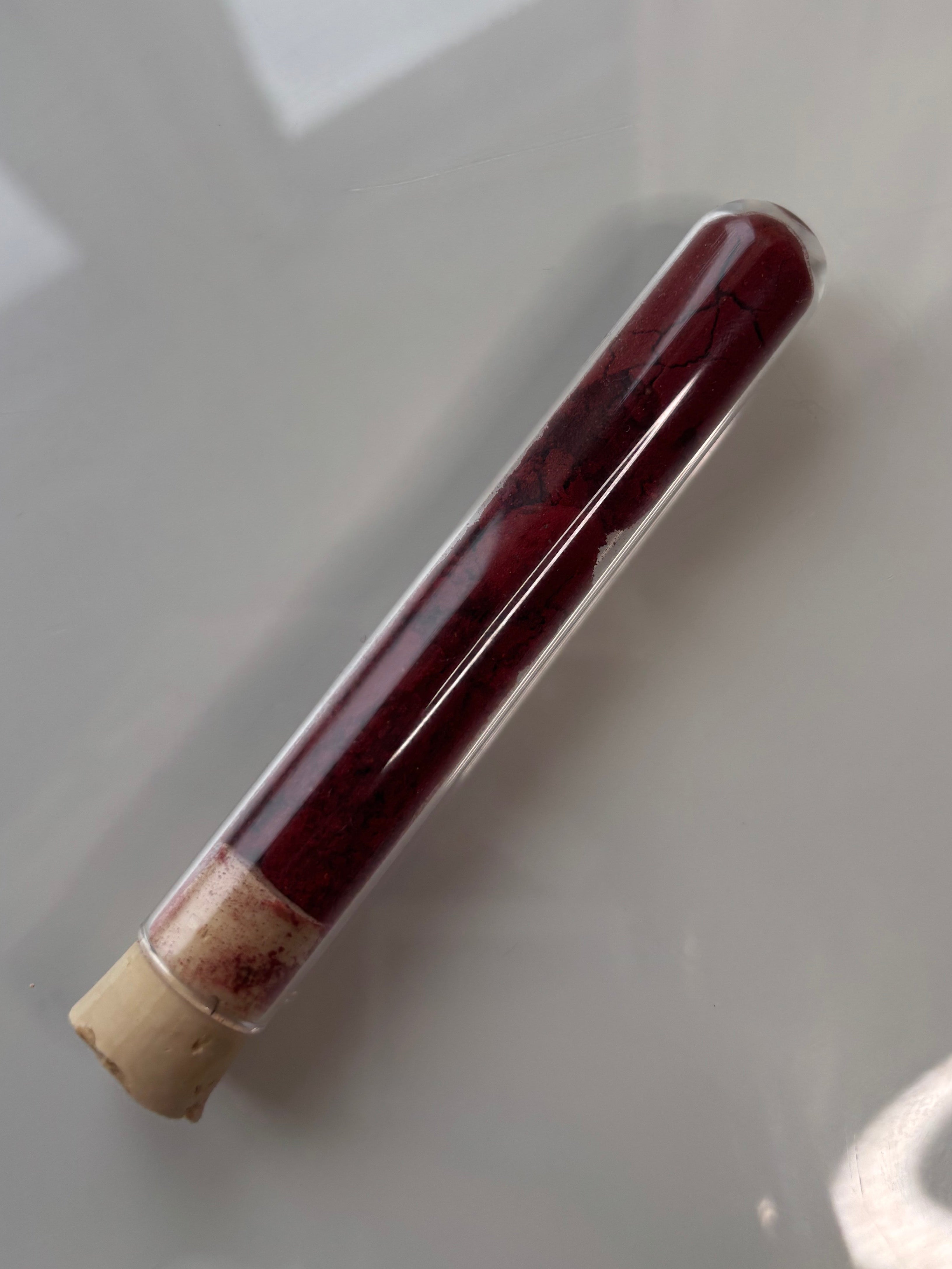 Packshot, Drachenblutpulver Harz  auf glänzendem Hintergrund in Glasröhrchen mit Korkverschluss